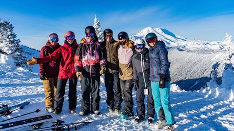 Group of skiers stand in front of Mt. Rainier in colorful snow clothing. 