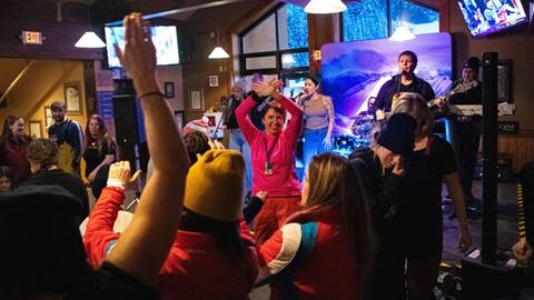 Woman dances in front of a crowd as a band plays on a stage in the background. 