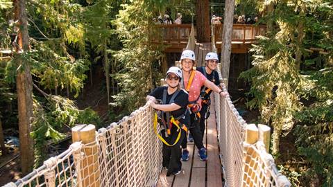 Three women smile as they cross a bridge at Crystal Mountain's Rope Course