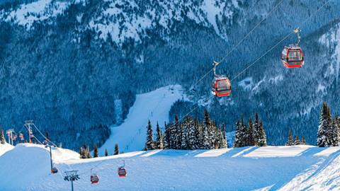 Two cabins ascend a snow covered peak as the camera looks down into a mountain valley.