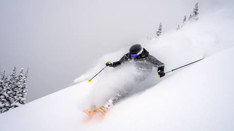 A skier carving through deep powder snow on a steep slope at Crystal Mountain Resort