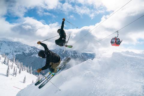 Two skiers perform freedride tricks in unison. 