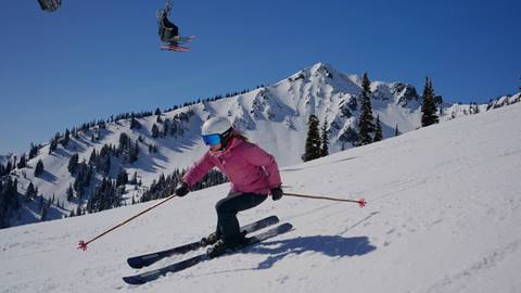Woman skier in pink jacket has perfect form skiing down the mountain. 