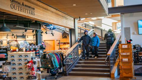 A couple walks down the stairs of Crystal Mountain Outfitters in snow gear. 