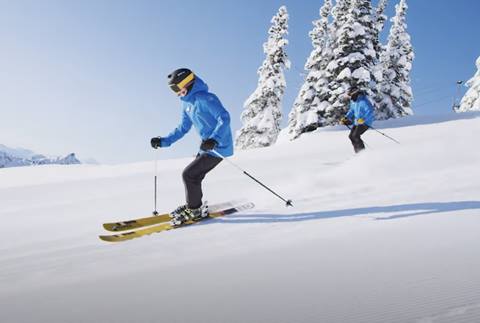 A skier and their instructor rip down the mountain. 