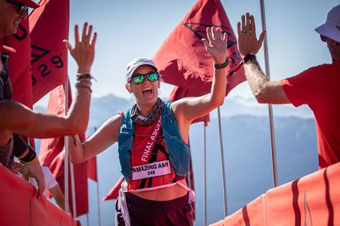 Woman gives other race participants high fives amidst orange race flags and the Cascade mountains in the background. 