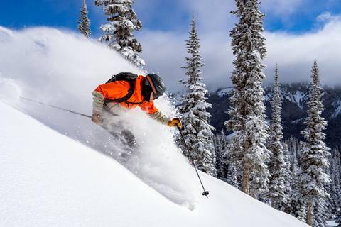 Skier in an orange parka shreds powder on a bluebird day. 