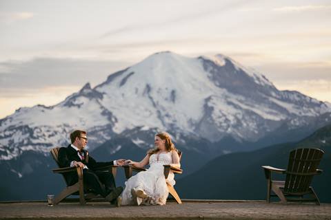 A married couple holds hands in a lounge chair with Mt. Rainier in the background. 