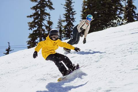 Two snowboarders carving down a snowy slope at Crystal Mountain